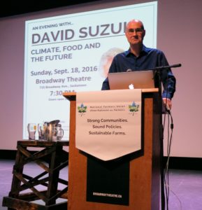Darrin Qualman speaking from a podium at a Saskatoon event featuring Dr. David Suzuki in 2016.
